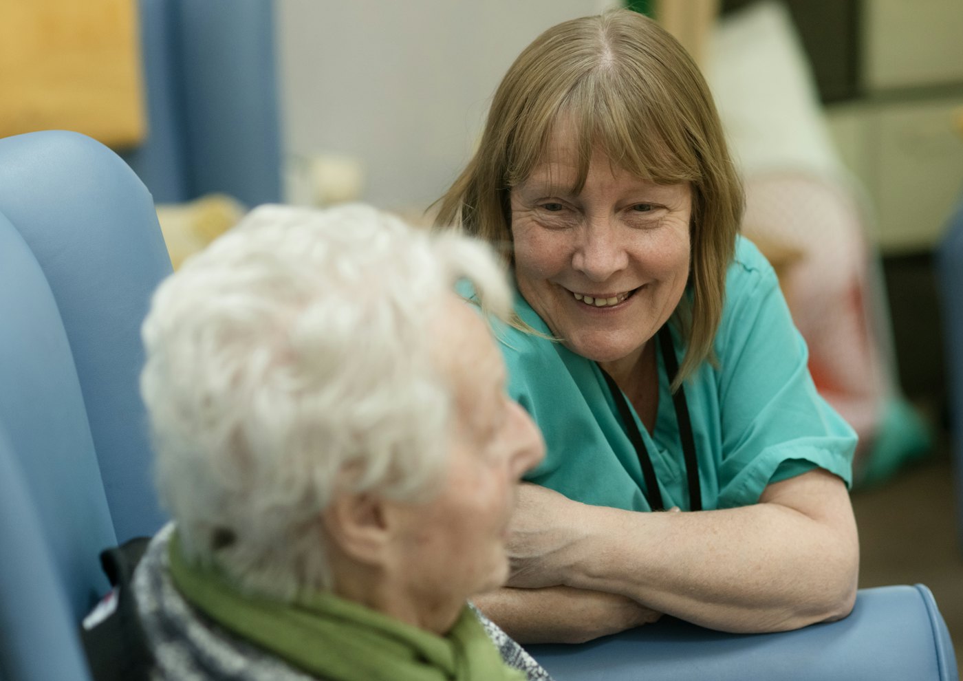 A caregiver leaning in to chat with a smiling older woman