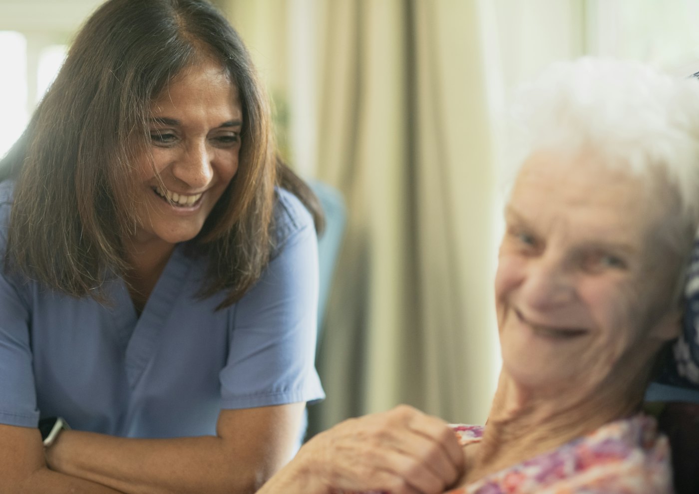 A smiling caregiver sitting with an older woman at home